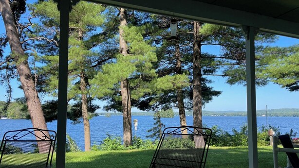 A covered outdoor seating area with metal chairs and a view of a lake surrounded by trees.