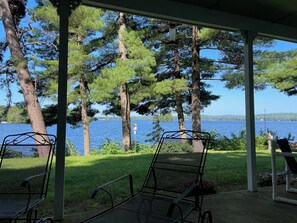 A covered outdoor seating area with metal chairs and a view of a lake surrounded by trees. - Charming New England 4bd Family Lake House w/ Yard, Patio, Docks and Views (Strafford)