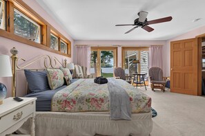 Un dormitorio con cama, mesitas de noche, ventilador de techo y vistas al exterior.