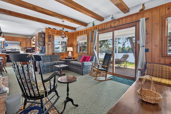 A cozy cabin interior with a living area, kitchen, and a sliding glass door leading to a deck.