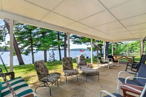 A covered patio with outdoor furniture, a swing, and a view of a lake. - Gorgeous New England 4bd Family Lake House w/ Large Yard, Patio, Docks and Views (Strafford)