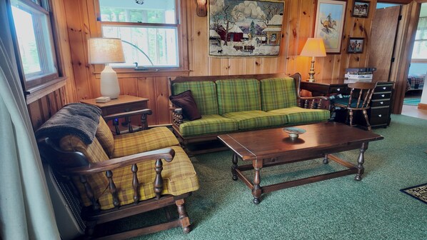 A cozy living room with a green plaid sofa, a wooden rocking chair, a wooden coffee table, and a lamp on a side table. - Charming New England 4bd Family Lake House w/ Yard, Patio, Docks and Views (Strafford)