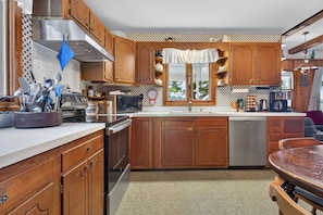 A kitchen with wooden cabinets, a stainless steel range hood, a microwave, and a dishwasher. - Gorgeous New England 4bd Family Lake House w/ Large Yard, Patio, Docks and Views (Strafford)
