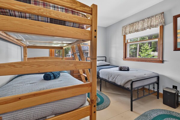 A dormitory room with bunk beds, a window with a view, and a small bedside table. - Gorgeous New England 4bd Family Lake House w/ Large Yard, Patio, Docks and Views (Strafford)