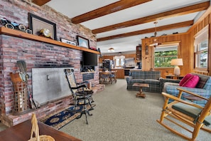 A cozy living room with a fireplace, wooden beams, and a dining area with a table and chairs.