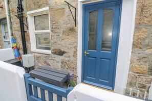 Un bâtiment en pierre avec une porte bleue, une fenêtre et un banc à l’extérieur.