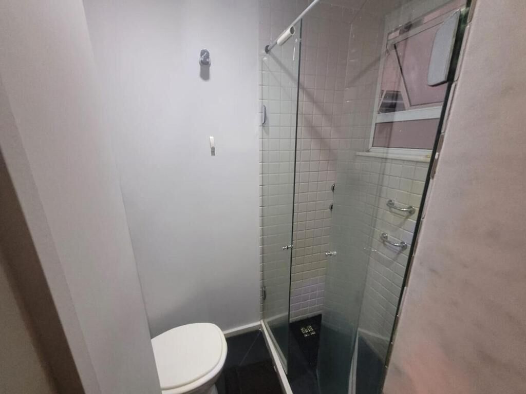 Une petite salle de bain fermée, comprenant des toilettes, une douche en verre et des murs carrelés.