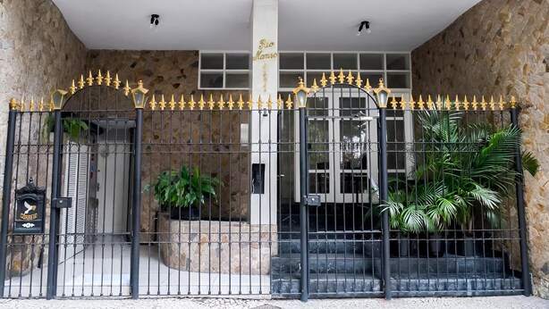 A gated entrance with a stone wall, a metal gate with golden accents, and potted plants.
