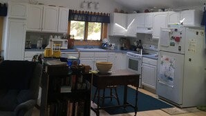 Une cuisine spacieuse avec des meubles blancs, un ventilateur de plafond, des fenêtres de toit et un réfrigérateur décoré d’aimants.