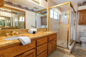 A bathroom with a granite countertop sink, wooden vanity, a glass-enclosed shower, and a toilet. - Fox Farm Manor (Big Bear Lake)