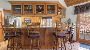 A kitchen with wooden cabinets, a central island with bar stools, and a view of the outside. - Fox Farm Manor (Big Bear Lake)