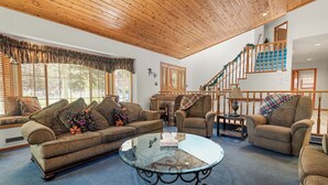 A spacious living room with a wooden ceiling, a glass coffee table, a sofa set, and a staircase with blue steps. - Fox Farm Manor (Big Bear Lake)