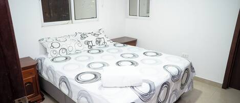 Une chambre à coucher comprenant un lit, deux tables de chevet, une armoire en bois et deux fenêtres.