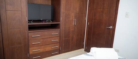 A bedroom with a bed, a wooden wardrobe, and a television on a shelf.