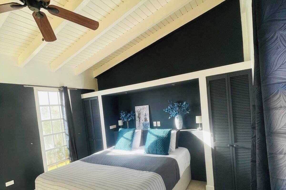 Een slaapkamer met een bed, plafondventilator, raam en deur.
