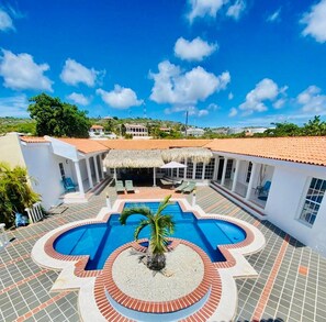 Ein Poolbereich mit kreisförmigem Design, umgeben von einem weißen Gebäude mit rotem Ziegeldach, und eine Palme in der Mitte.