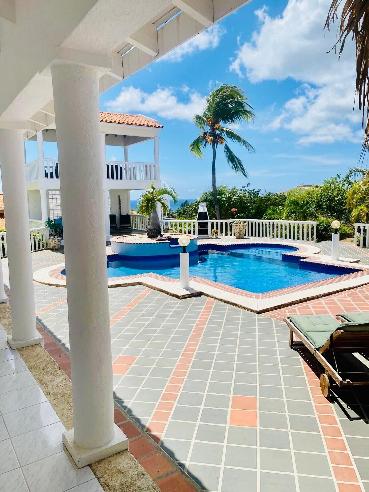 A pool area with tiled flooring, lounge chairs, and a view of a building with a balcony.