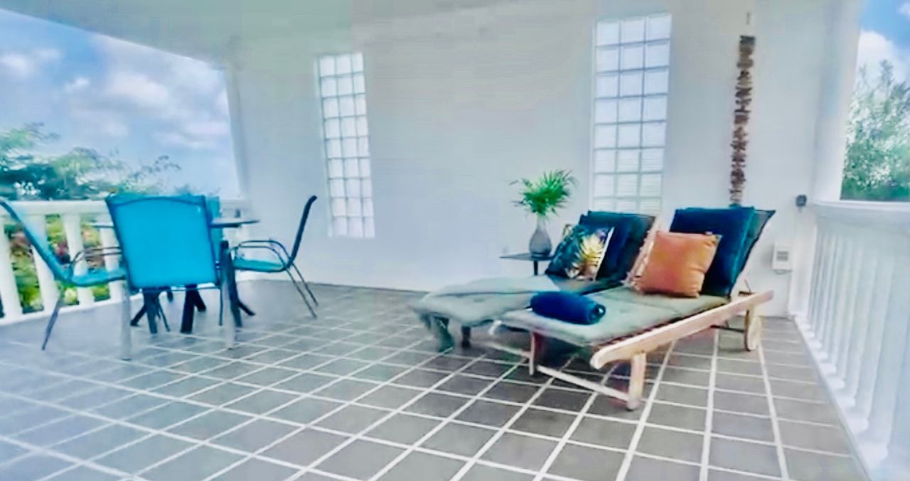 A covered patio area with a table and chairs, a cushioned bench, and a potted plant.