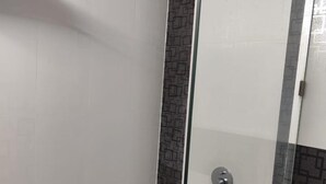 A modern shower with a glass door, a handheld showerhead, and a wall-mounted faucet. - Airport City Hotel (Barakpur)