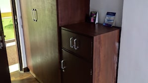 A room with a wooden wardrobe, a small desk with a book and a brochure, and a door leading to an outdoor area. - Airport City Hotel (Barakpur)