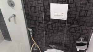 A small bathroom with a toilet, a shower, and a towel dispenser. - Airport City Hotel (Barakpur)