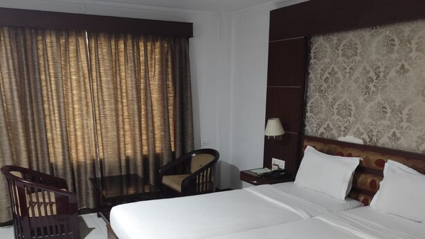 A hotel room with a large bed, a desk, a chair, and a patterned rug. - Airport City Hotel (Barakpur)
