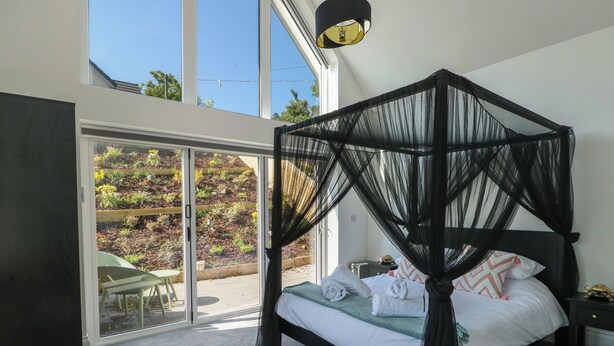 Una camera da letto moderna con un letto a baldacchino, una porta scorrevole in vetro su un giardino e un'ampia finestra.