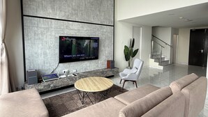 A modern living room with a flat-screen TV mounted on a textured wall, a round wooden coffee table, and a beige sofa.