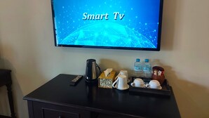 Een tv waarop 'Smart Tv' staat, met een koffiezetapparaat, twee waterflessen en een afstandsbediening op een donker houten tafel.