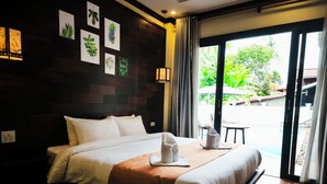 Een hotelkamer met een groot bed, een klein tafeltje met een stoel, en uitzicht op een zwembad en groen.