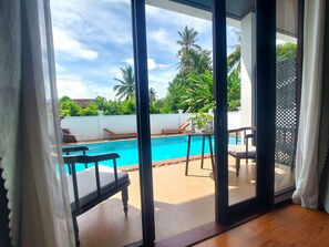 Vista desde una habitación con puerta de cristal a un área de piscina, que incluye piscina, sillones de descanso y una planta en maceta.