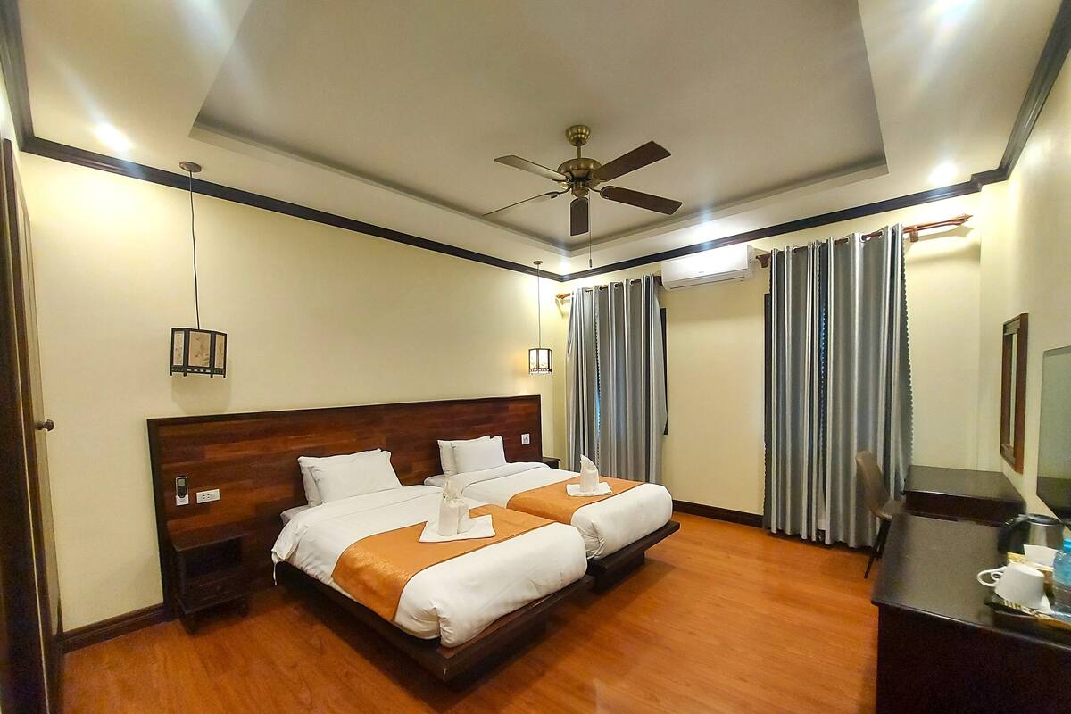 Ein Hotelzimmer mit zwei Betten, einem Deckenventilator, einem Schreibtisch und einem Fernseher.