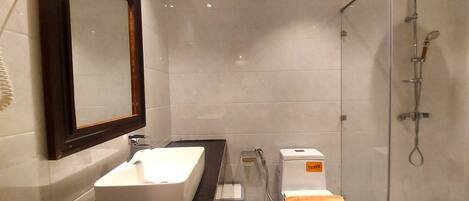 Une salle de bain avec un grand miroir, un lavabo blanc, des toilettes et une douche.