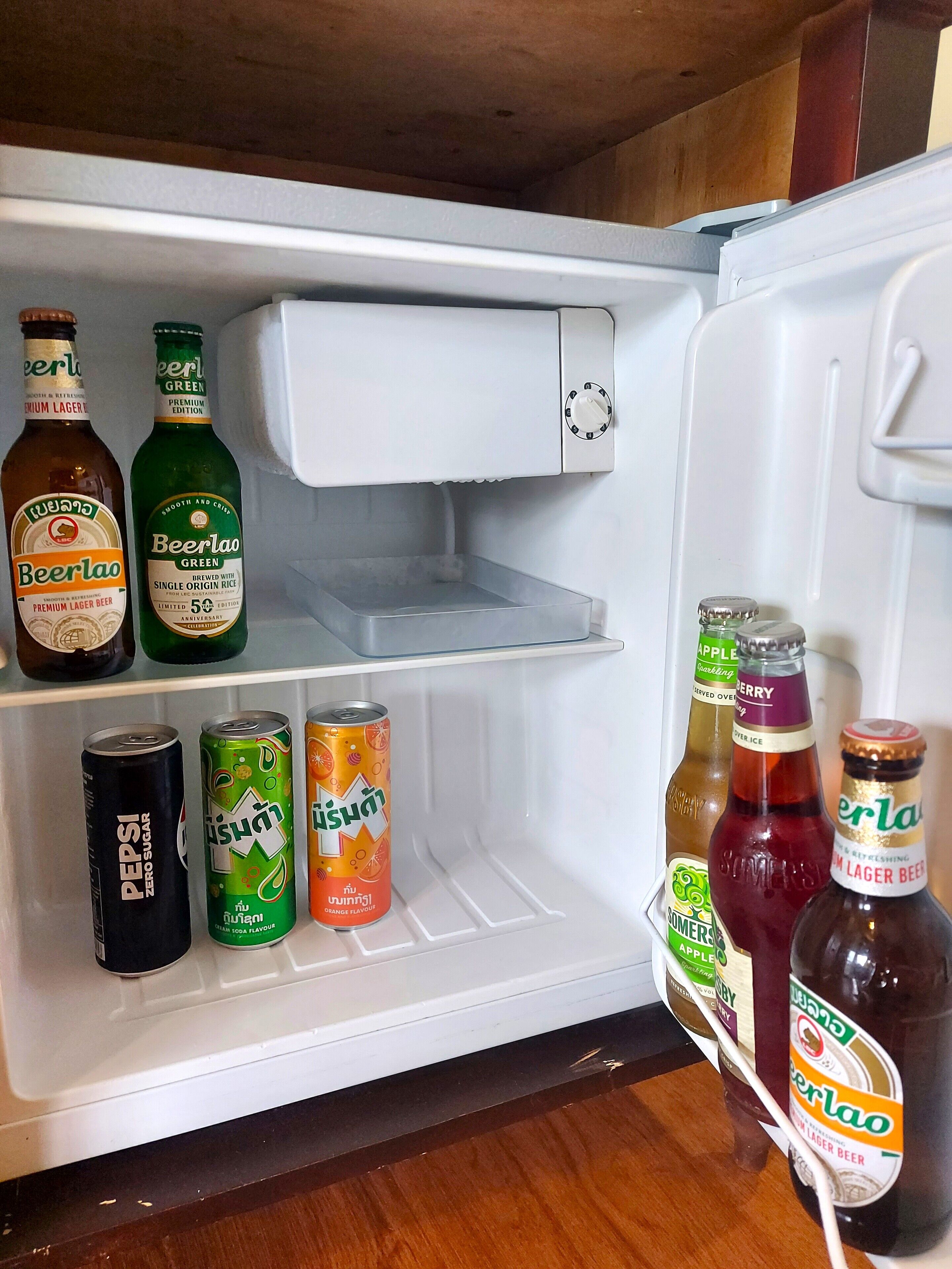 Een open koelkast met verschillende drankjes, waaronder bier, frisdrank en vruchtensap.