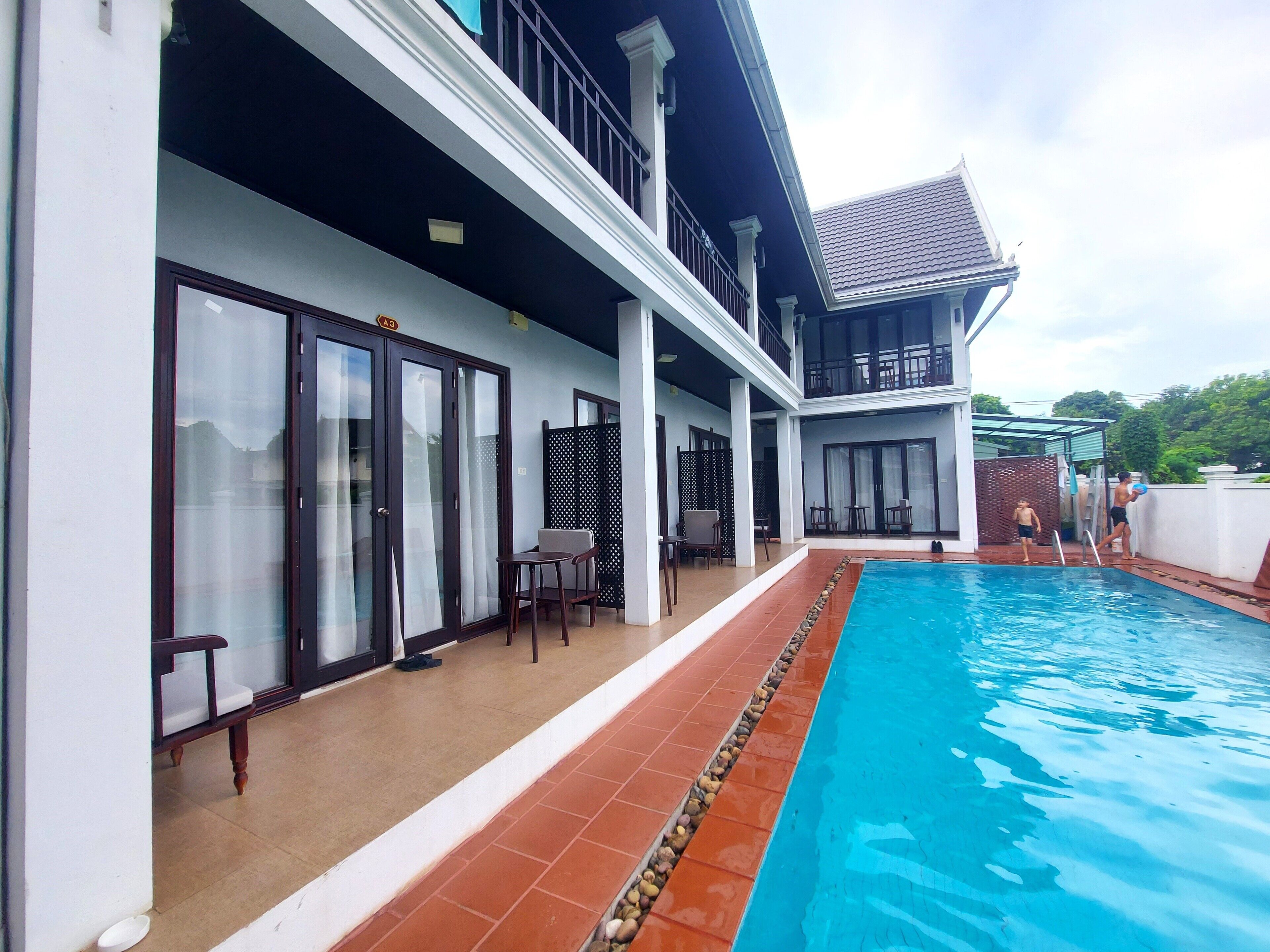A two-story building with a swimming pool, outdoor seating, and a covered patio area.