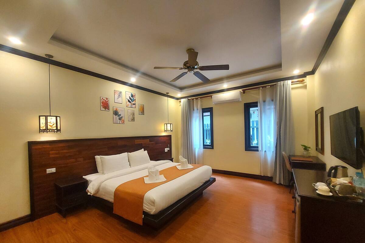 Ein Hotelzimmer mit einem großen Bett, einem Deckenventilator, Kunstwerken an den Wänden und einem Fernseher auf einer Kommode.