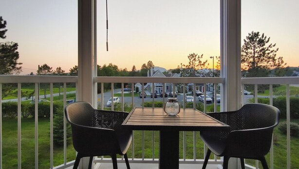 Een balkon met een tafel en twee stoelen, met uitzicht op een parkeerplaats en huizen.