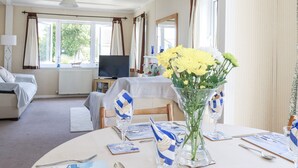 Ett hotellrum med en säng, en tv, ett matbord med en vas med blommor och utsikt över omgivningarna.