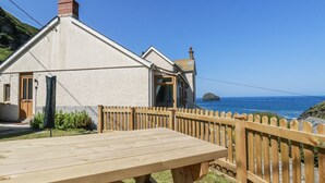 Ett hus vid kusten med en träveranda och ett bord, med utsikt över havet.