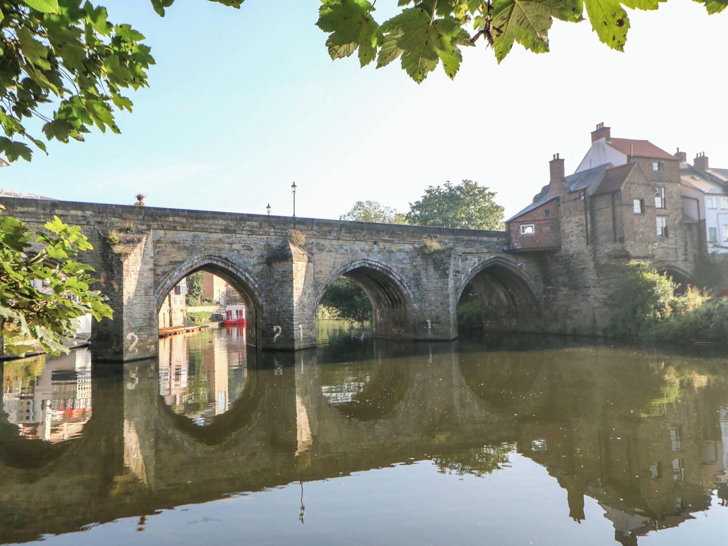 Un puente de piedra sobre un río tranquilo, con el reflejo del puente y edificios.