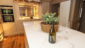A modern kitchen with white cabinetry, a marble countertop, a built-in oven, and a dining area with a wicker basket and wine glasses. - White House (Durham)