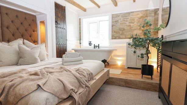 A bedroom with a large bed, a wooden headboard, a stone wall, a bathtub, and a potted plant. - White House (Durham)