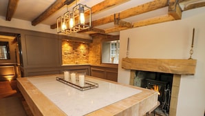 A spacious kitchen with a large island, exposed wooden beams, a stone accent wall, and a fireplace. - White House (Durham)