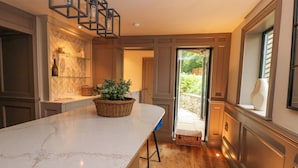 A kitchen with a marble countertop, wicker baskets, and a view to the outside. - White House (Durham)