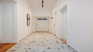 Un couloir avec un sol à motifs, des murs blancs et une porte au fond.