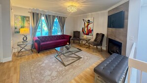 Ein Wohnzimmer mit einem roten Sofa, zwei Sesseln, einem Glastisch, einem Kamin und einem großen abstrakten Gemälde.