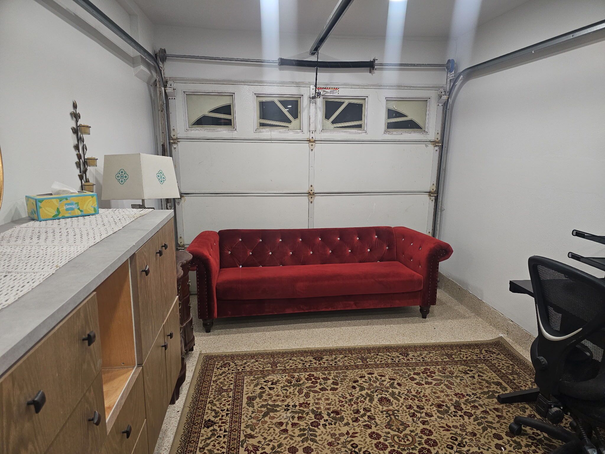 Ein Zimmer mit einem roten Samtsofa, Holzschränken, einem gemusterten Teppich und einem Schreibtisch mit Lampe und Taschentüchern.