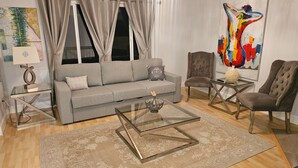 Ein Wohnzimmer mit grauem Sofa, zwei Sesseln, einem Glastisch und einem gemusterten Teppich.