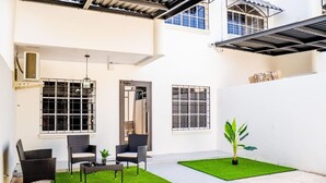 A clean, modern outdoor patio area with wicker furniture, artificial grass, and a potted plant.