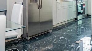 A modern kitchen with a stainless steel refrigerator, a microwave, and a glass dining table.